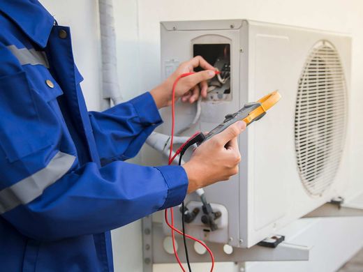 Electricista con ropa de trabajo verde que usa un destornillador para trabajar en un panel eléctrico con cables e interruptores.