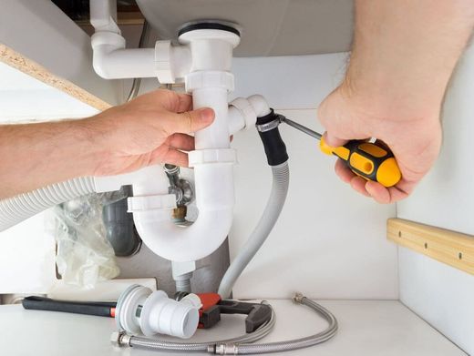 Electricista con ropa de trabajo verde que usa un destornillador para trabajar en un panel eléctrico con cables e interruptores.