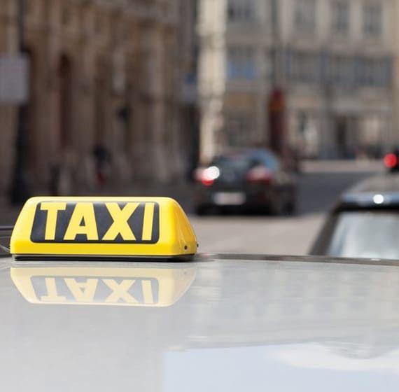 Panneau jaune « TAXI » sur le toit d'une voiture, rue de la ville en arrière-plan, voitures floues.