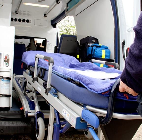 Intérieur d'une ambulance avec un brancard, des fournitures et une personne tenant la poignée.