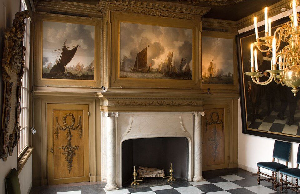 Ornate room with carved wood paneling, fireplace, large paintings, chandelier, and checkered floor