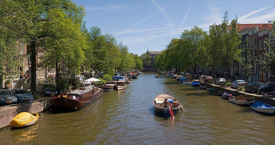 Canal lined with trees, parked boats, and bicycles on a sunny day in a city neighborhood