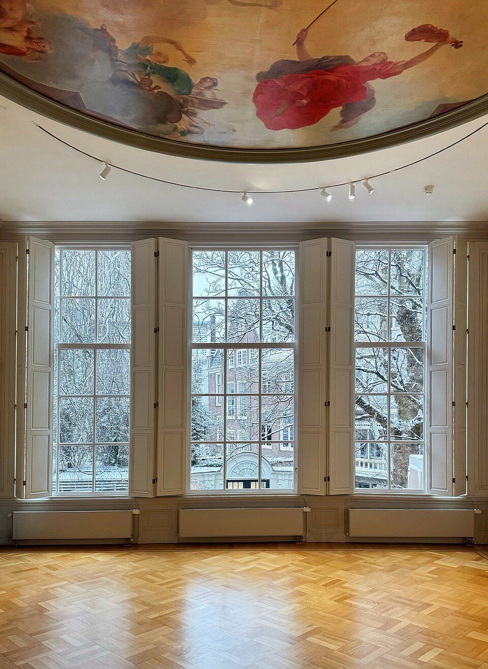Sunlit room with large frosted windows, hardwood floor, and a painted ceiling mural