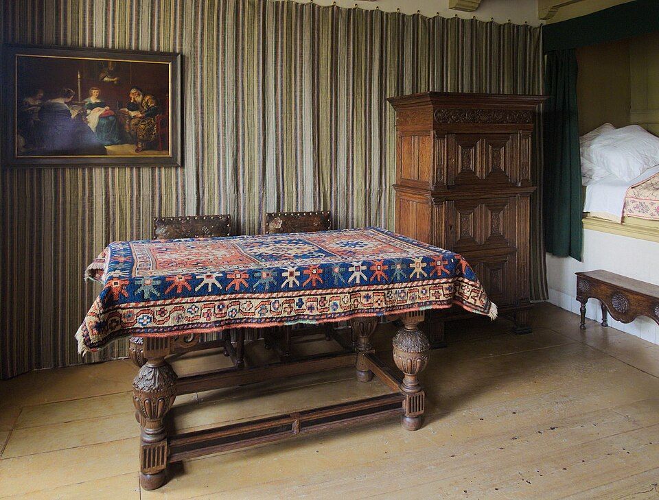 Traditional room with a patterned tablecloth on a carved wooden table, cabinet, and framed painting against striped walls