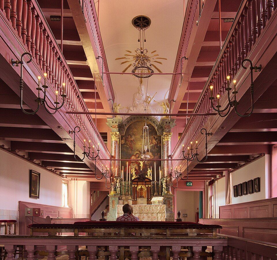Wide church interior with pews, a central altar, and ornate chandeliers under a high ceiling.