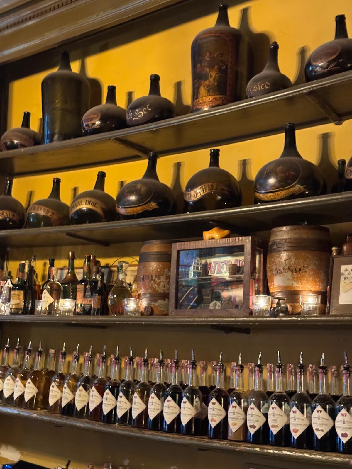 Shelves of antique pottery and bottles in a warmly lit bar display
