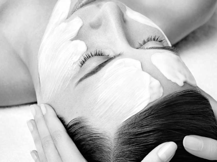 Una mujer con una toalla envuelta alrededor de su cabeza se aplica una crema en la cara.