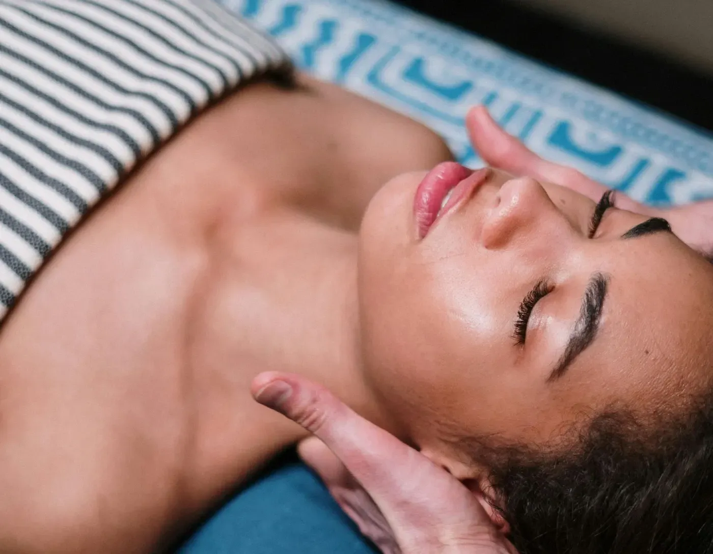 Una mujer acostada en una cama con los ojos cerrados recibiendo un masaje.