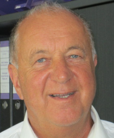 Mann mit kurzen Haaren und hellen Augen lächelt, er trägt ein weißes Hemd; Innenraum.