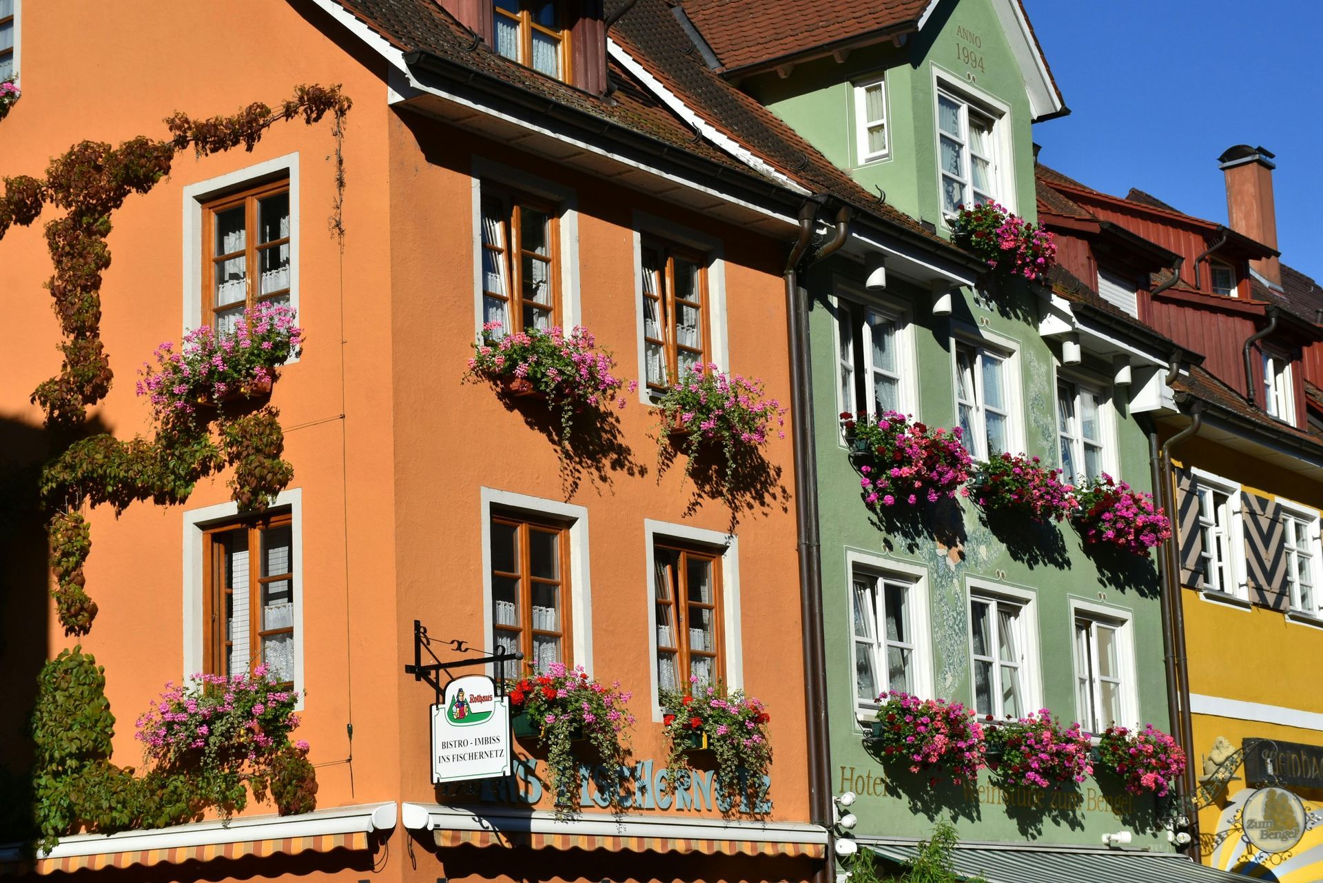 Farbenfrohe Gebäude mit Blumenkästen in einer europäischen Stadt, mit orangefarbenen, grünen und gelben Fassaden.