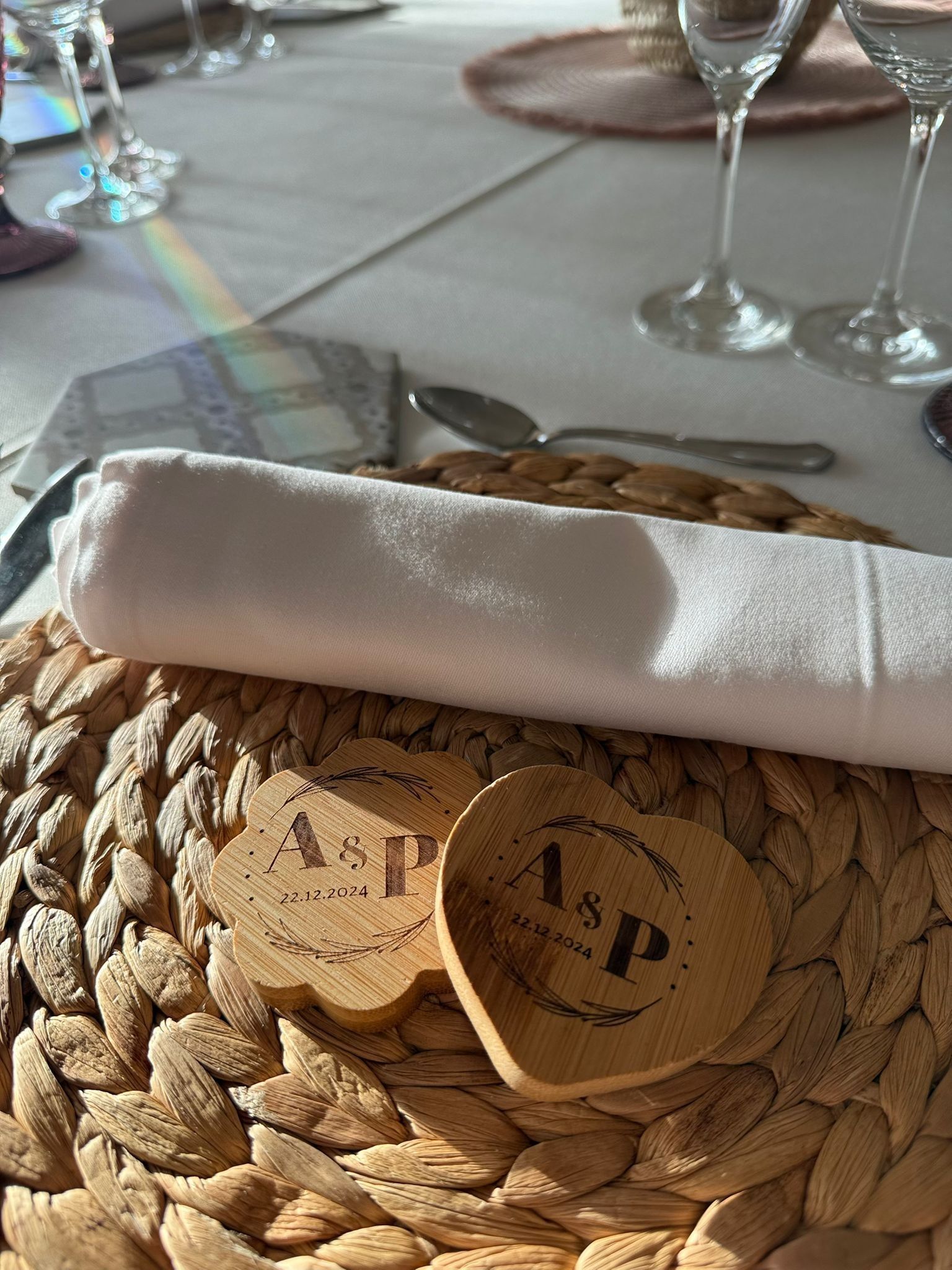 La mesa, de estilo formal, está puesta con un mantel individual tejido, una servilleta de lino blanco y dos obsequios de madera personalizados en forma de corazón.