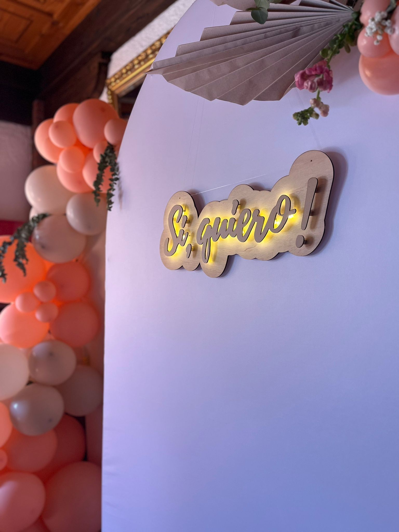 Un telón de fondo rosa claro para el evento, decorado con globos color melocotón y un letrero de neón brillante que dice 