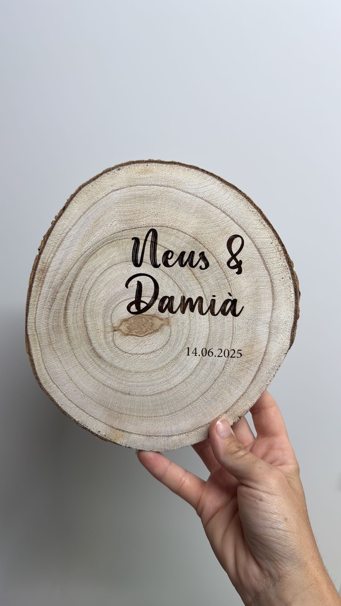 Una mano sostiene una rodaja circular de madera grabada con los nombres 