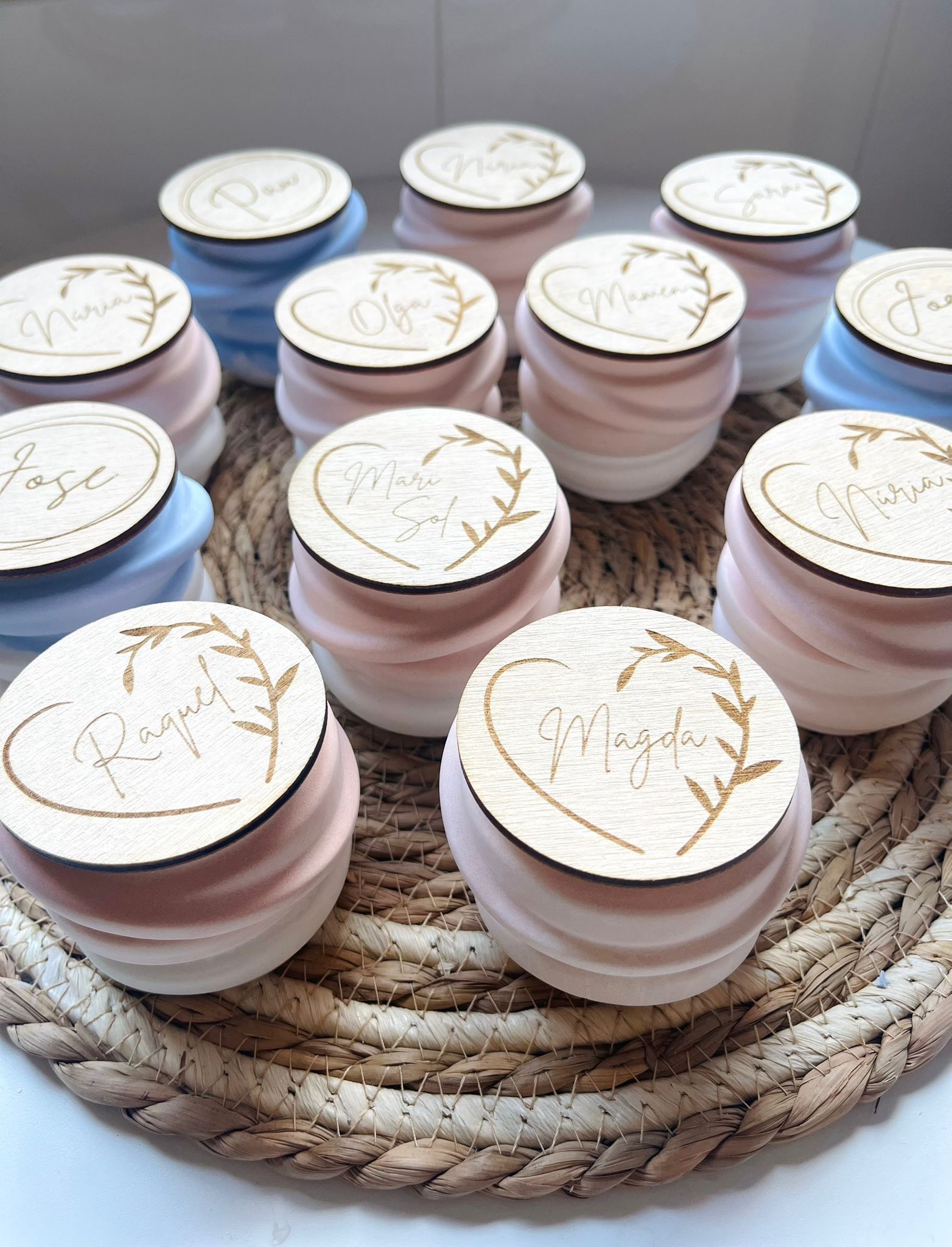 Malvaviscos de colores pastel apilados y coronados con discos de madera personalizados con diseños de corazones, dispuestos sobre una estera tejida.