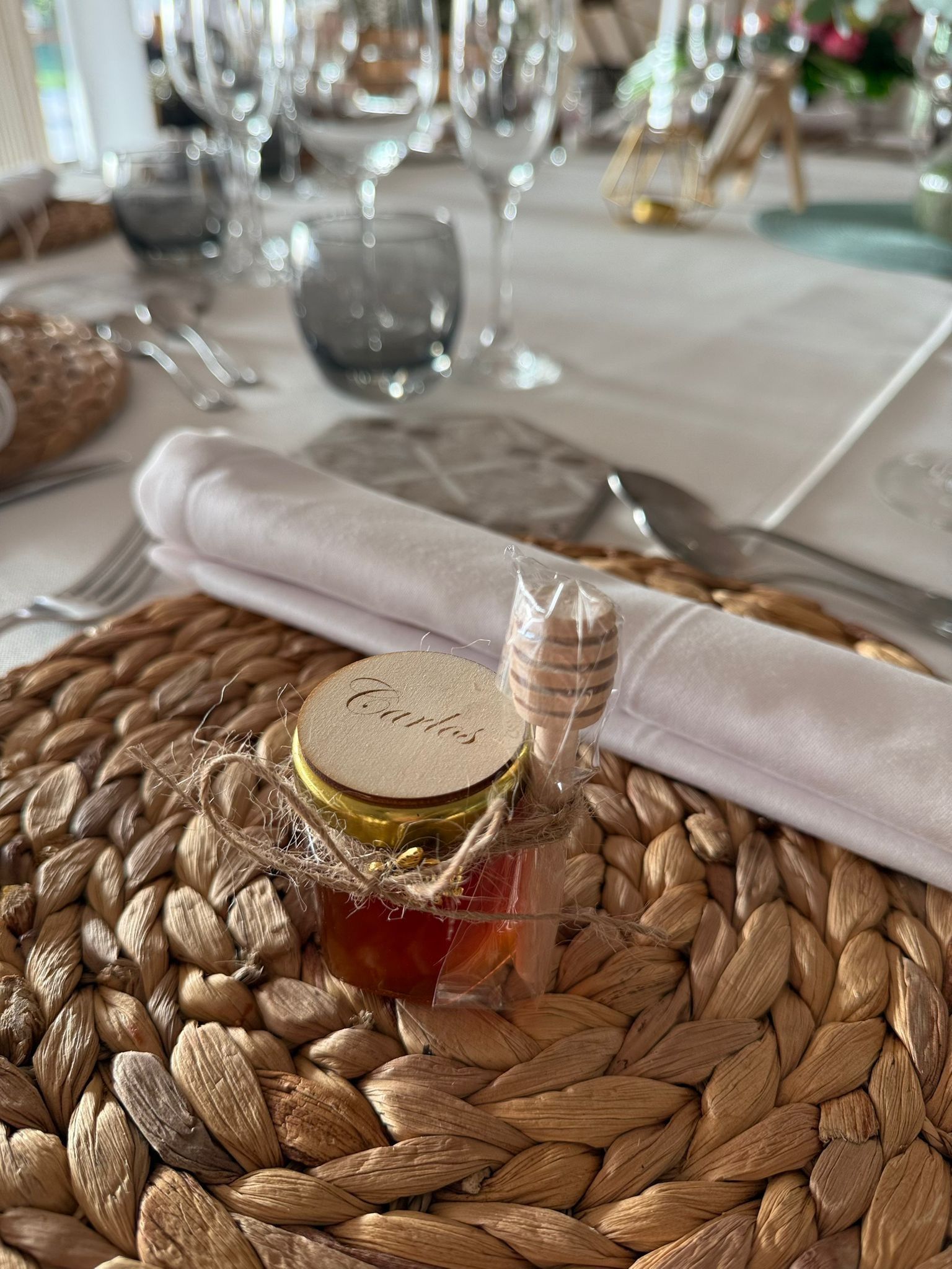 Un pequeño tarro de miel con un cucharón de madera sobre un mantel individual redondo tejido en una mesa formal.