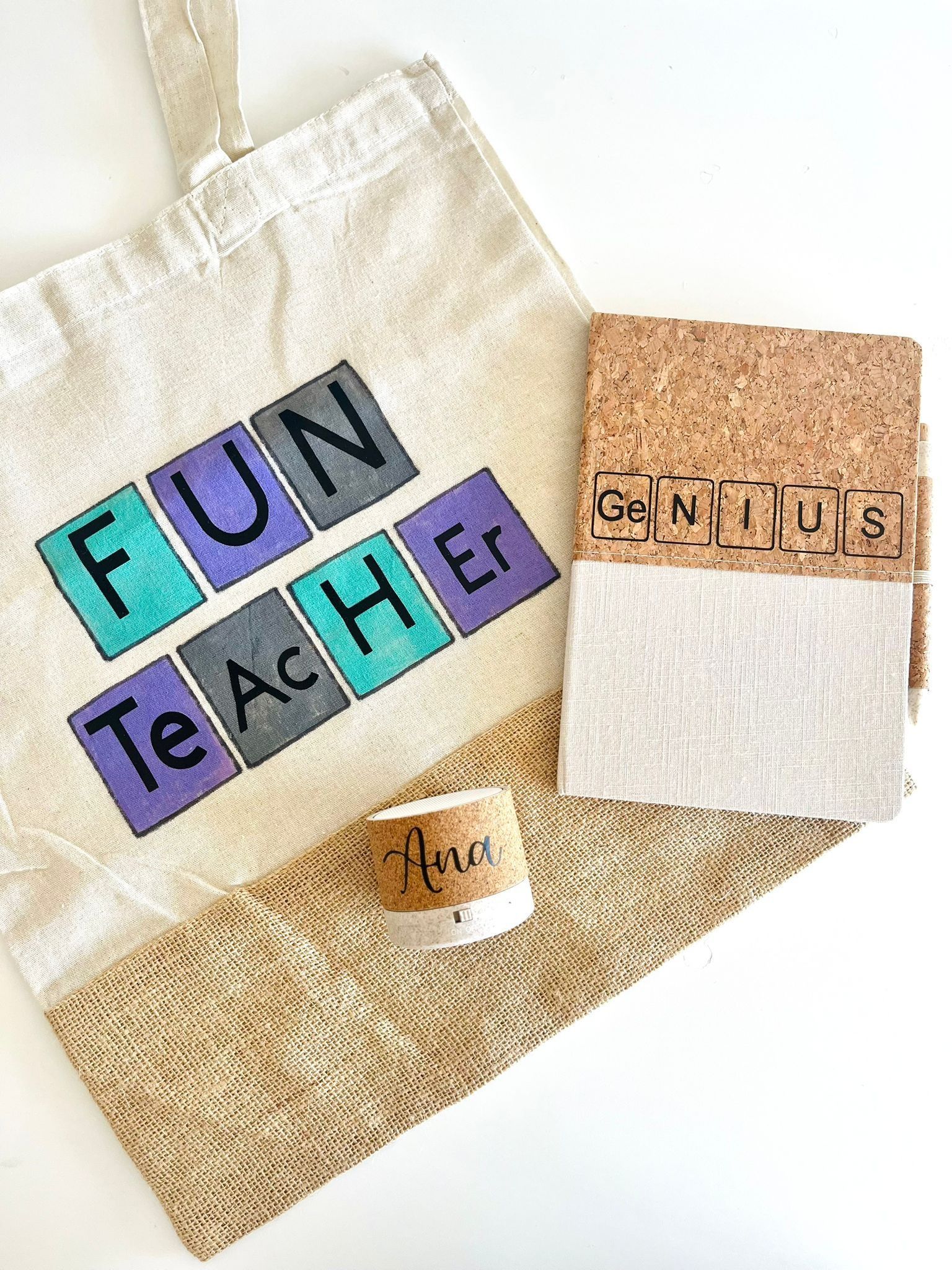 Una bolsa de tela, una libreta con cubierta de corcho y una pequeña vela de corcho, todas con diseños de texto con temática de profesores sobre un fondo blanco.