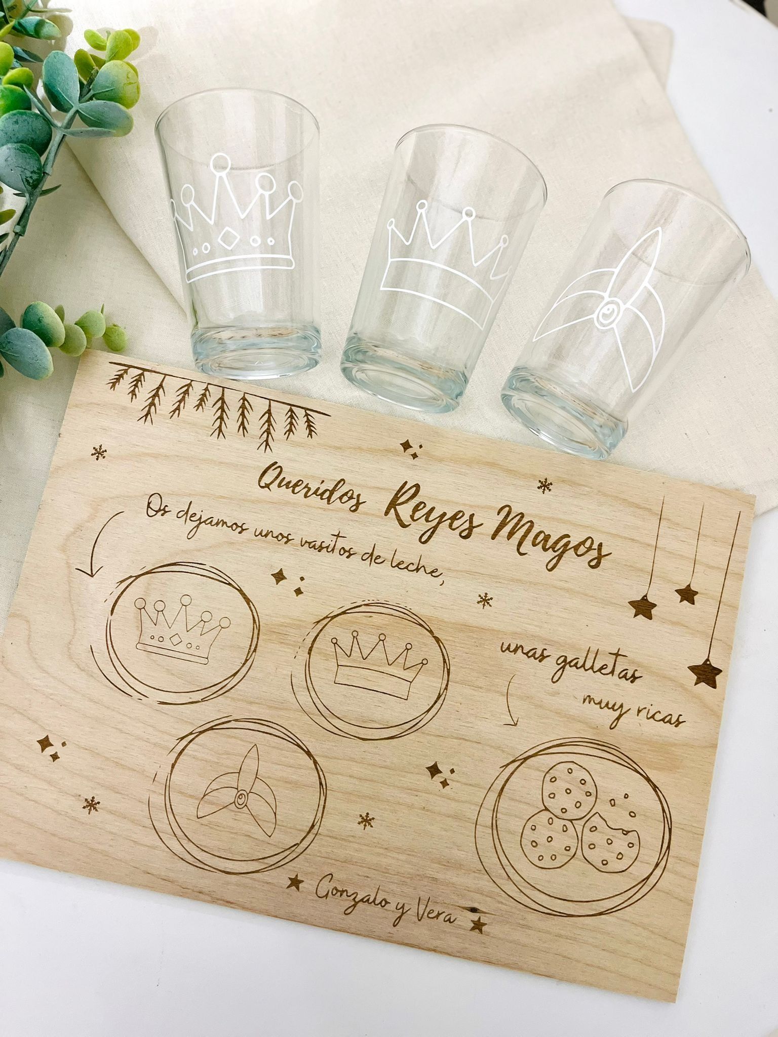 Tres vasos con grabados de coronas reposan sobre una tabla de madera grabada con 