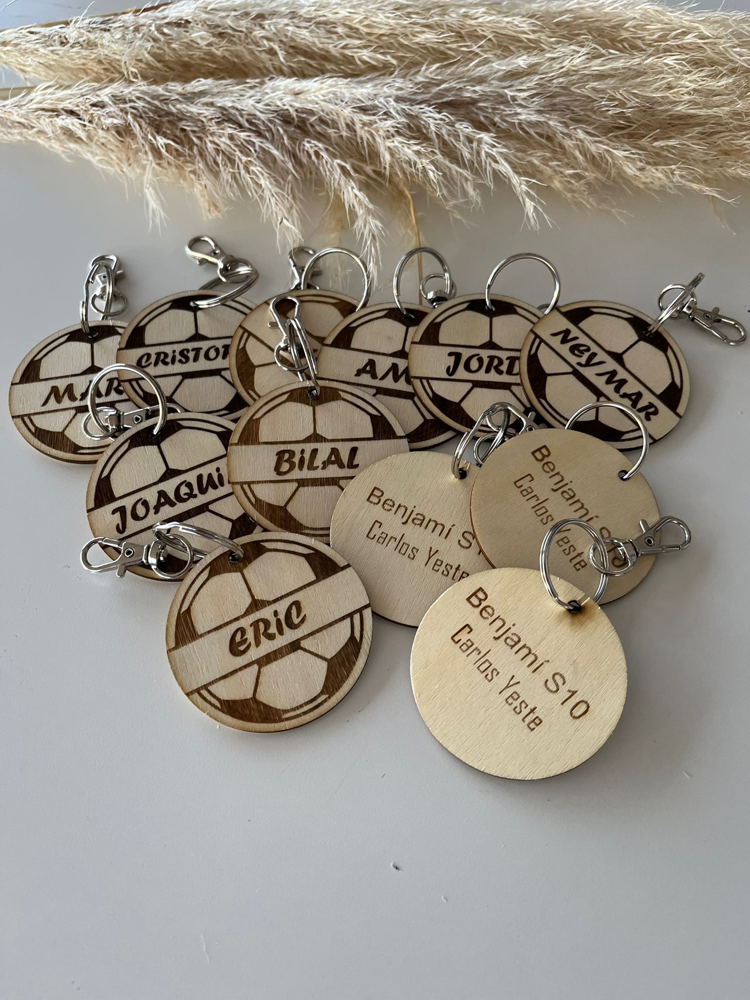 Una colección de llaveros circulares de madera con forma de balón de fútbol, ​​grabados con láser y con nombres personalizados, que reposan sobre una superficie blanca.