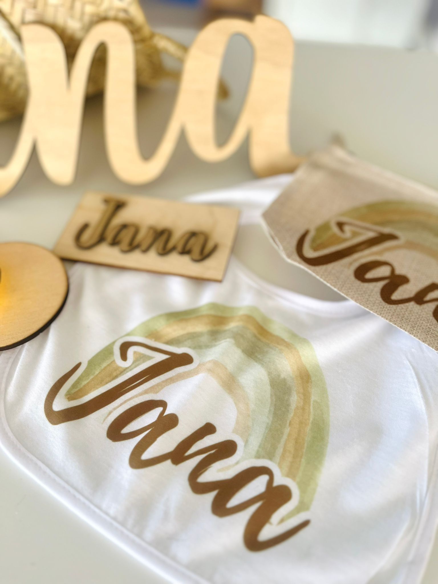 Un babero blanco con un dibujo de arcoíris y el nombre 