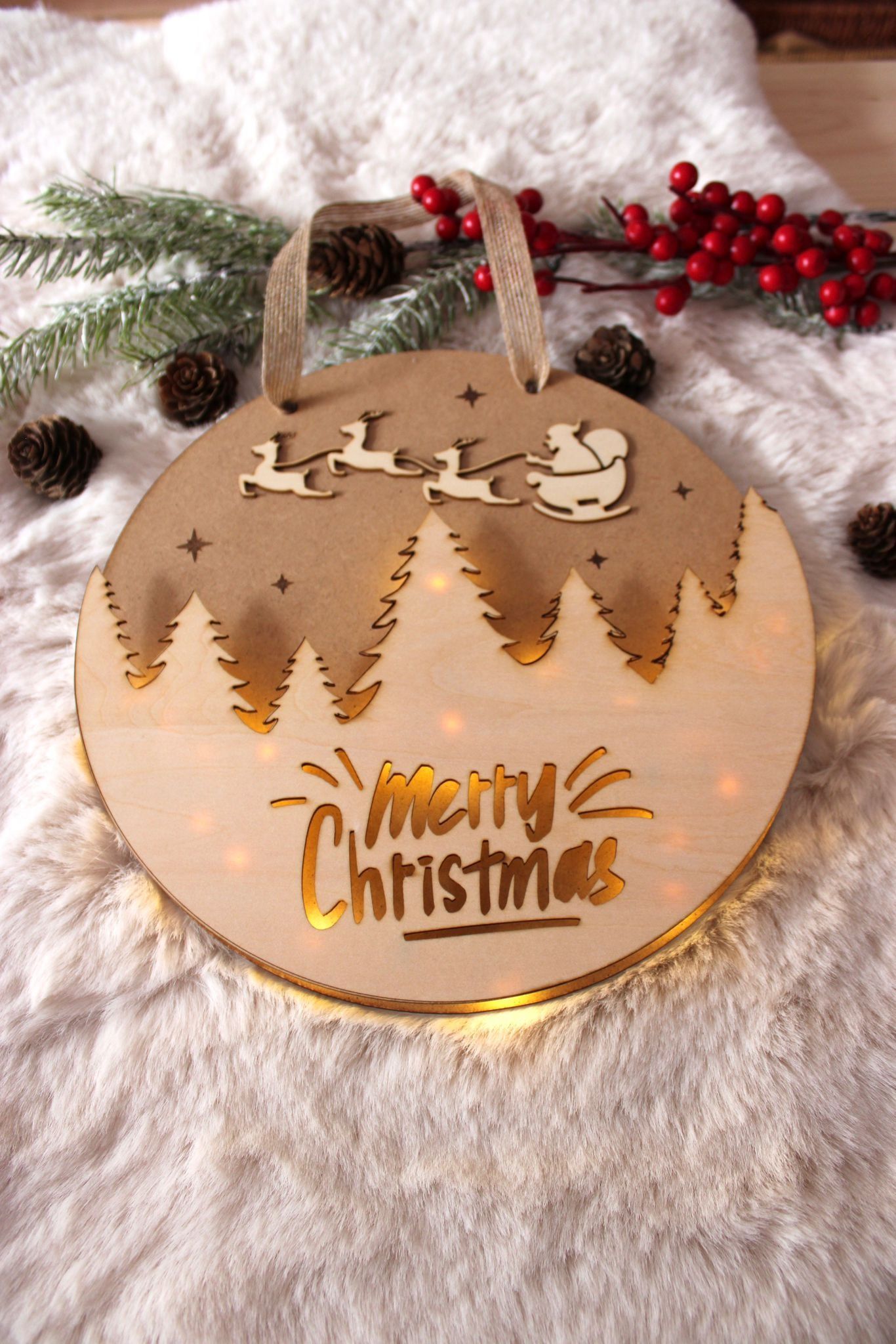 Adorno navideño circular de madera con luz, que presenta la silueta de un bosque, Papá Noel y sus renos, y la frase 