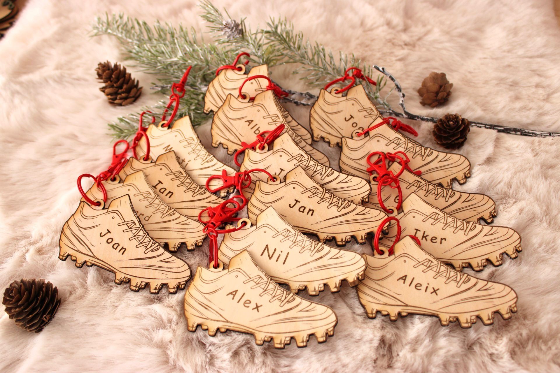 Varios adornos de madera con forma de zapato, cada uno grabado con un nombre diferente, dispuestos sobre una superficie blanca, peluda y texturizada.