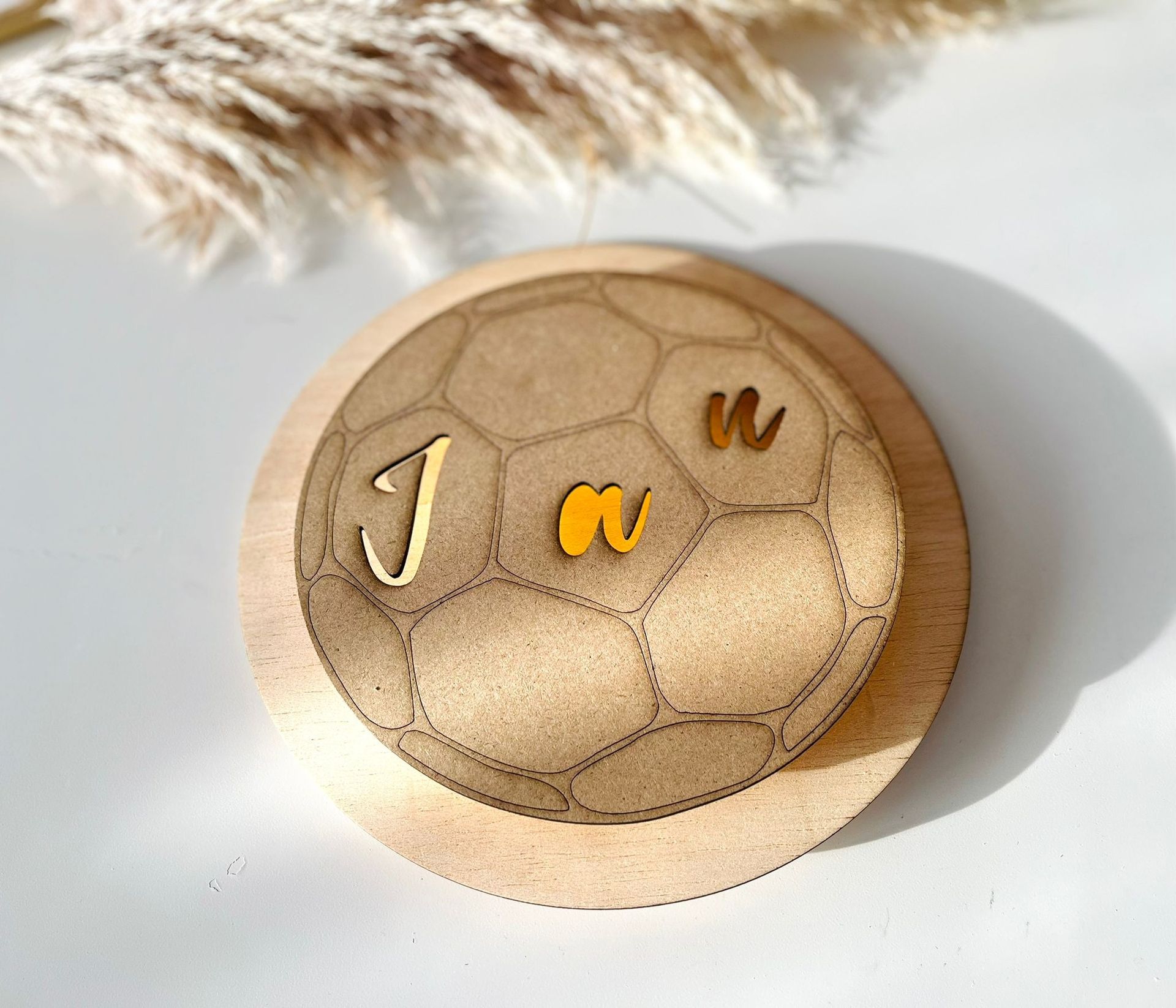 Un adorno de madera con forma de balón de fútbol, ​​con letras cursivas doradas que forman la palabra 
