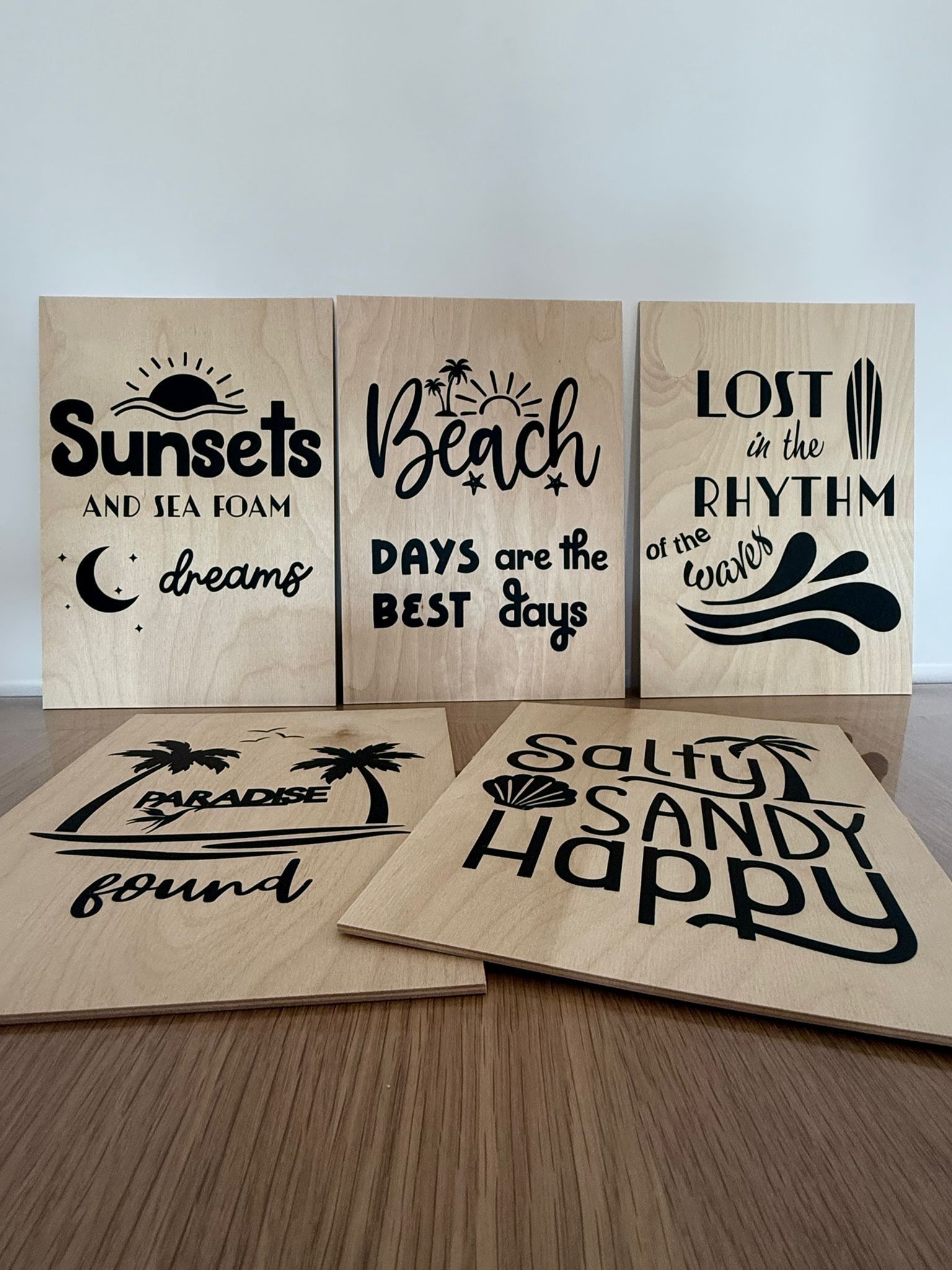 Cinco tablones de madera con tipografía y gráficos de temática playera en color negro, dispuestos sobre una mesa.