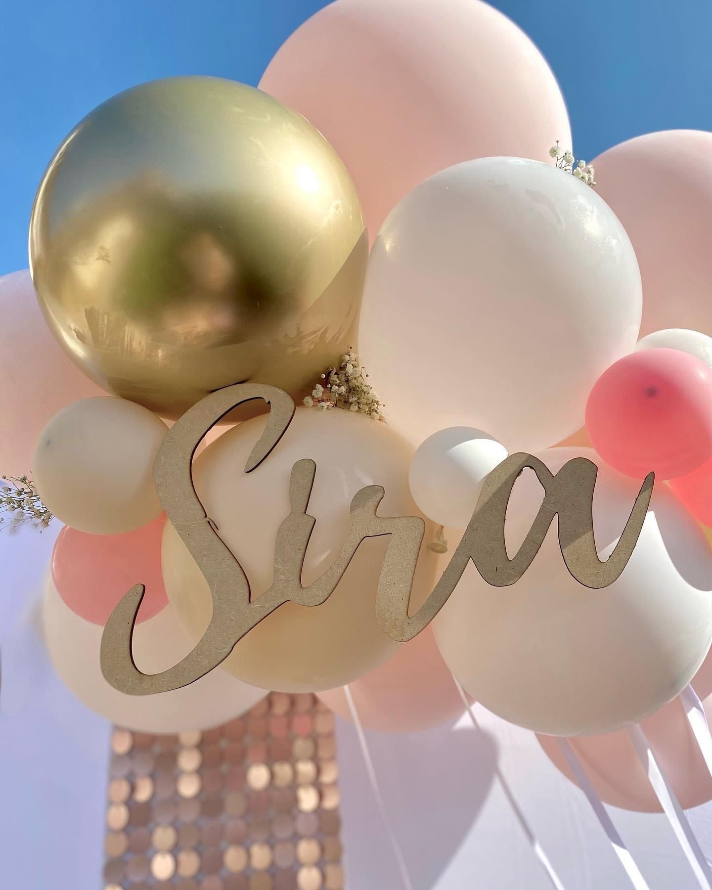 Un grupo de globos blancos, dorados y rosa pálido con un letrero dorado recortado que dice 