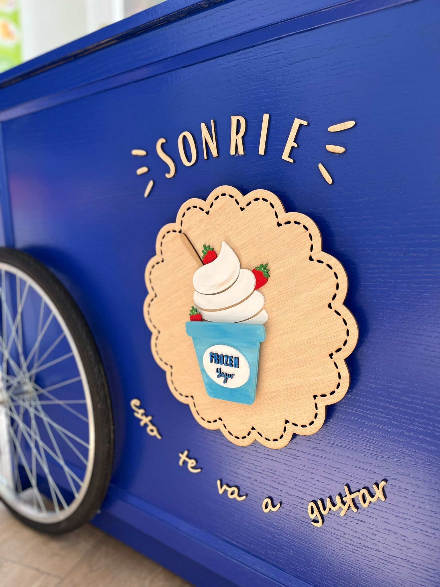 Un lateral azul del carrito con un recorte de corcho beige de un yogur helado de fresa con el texto en español 