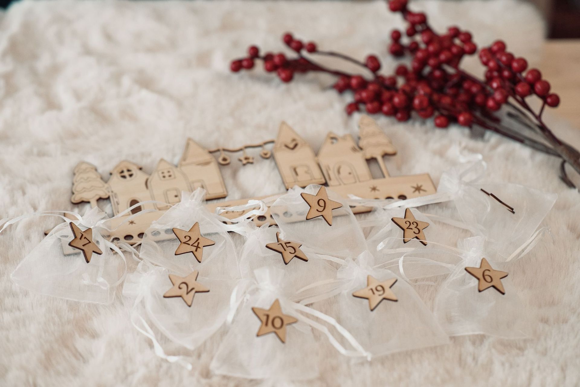 Un calendario de adviento navideño con pequeñas etiquetas numeradas en forma de estrella sobre bolsitas de organza blanca, sobre un fondo difuminado con bayas.