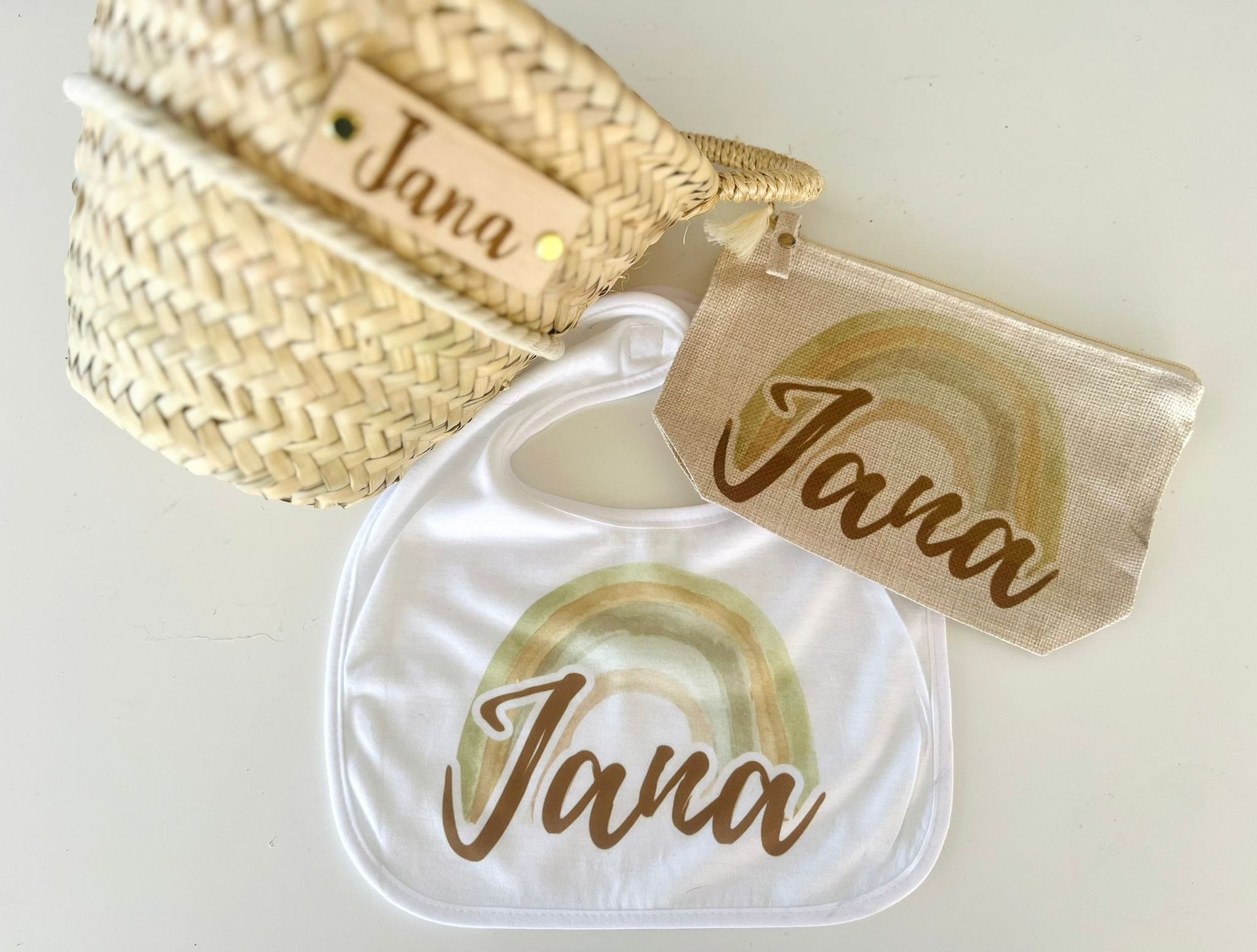 Una cesta tejida, un babero blanco y una bolsita con cremallera, todo personalizado con el nombre 