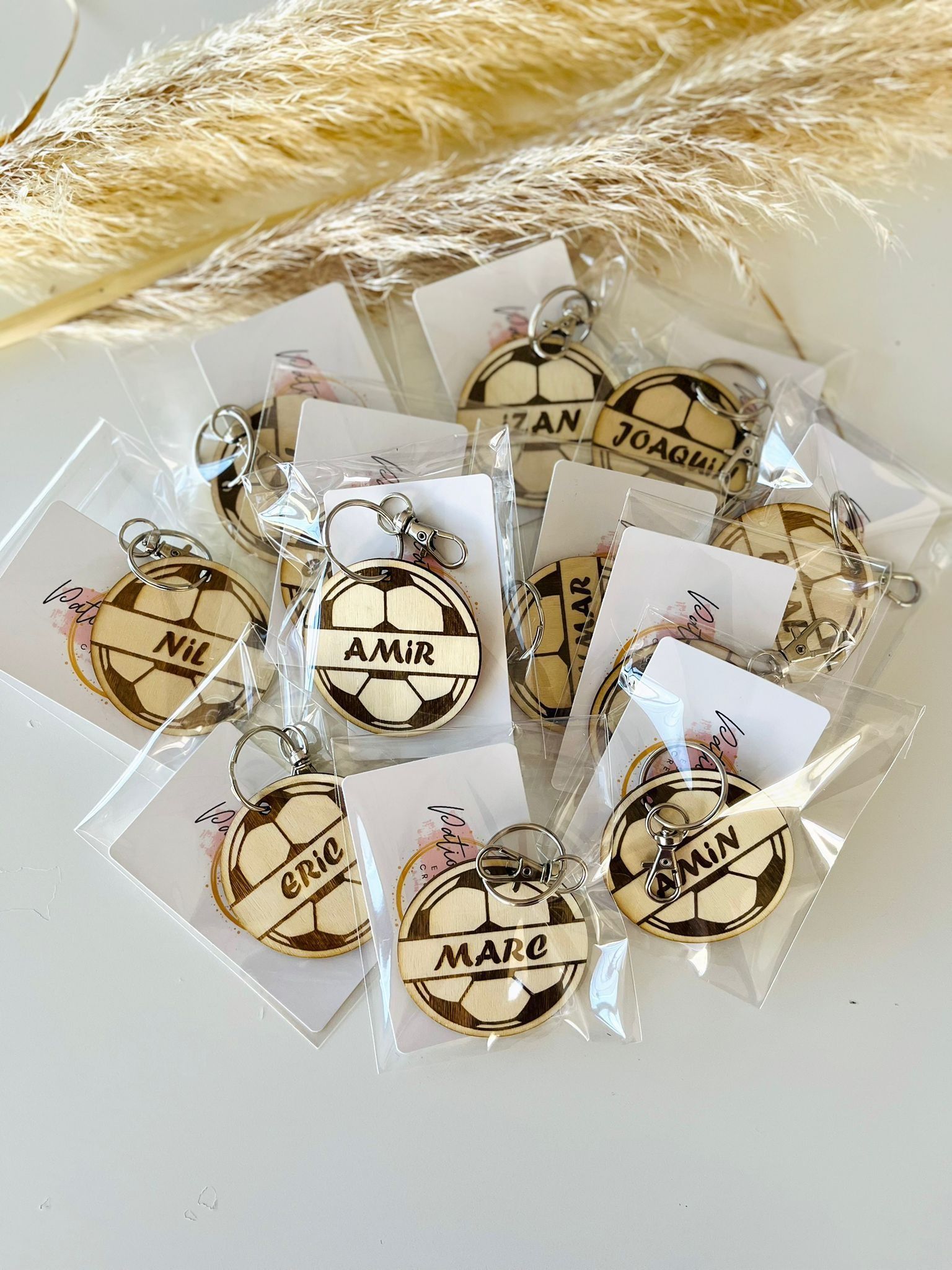 Un grupo de llaveros de madera personalizados con forma de balón de fútbol, ​​cada uno envuelto individualmente en un embalaje de plástico transparente.