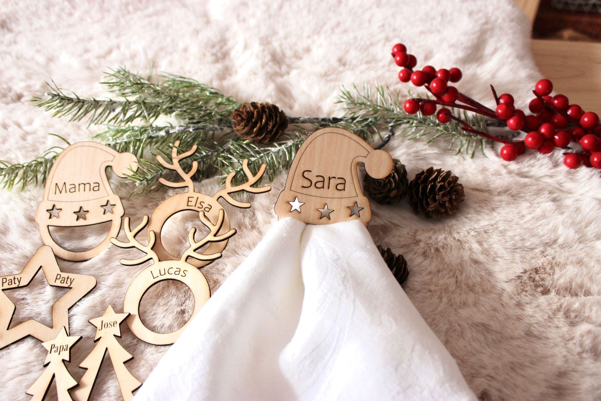 Servilleteros navideños de madera cortados con láser, con nombres, estrellas, gorros de Papá Noel y diseños de renos sobre una alfombra texturizada.