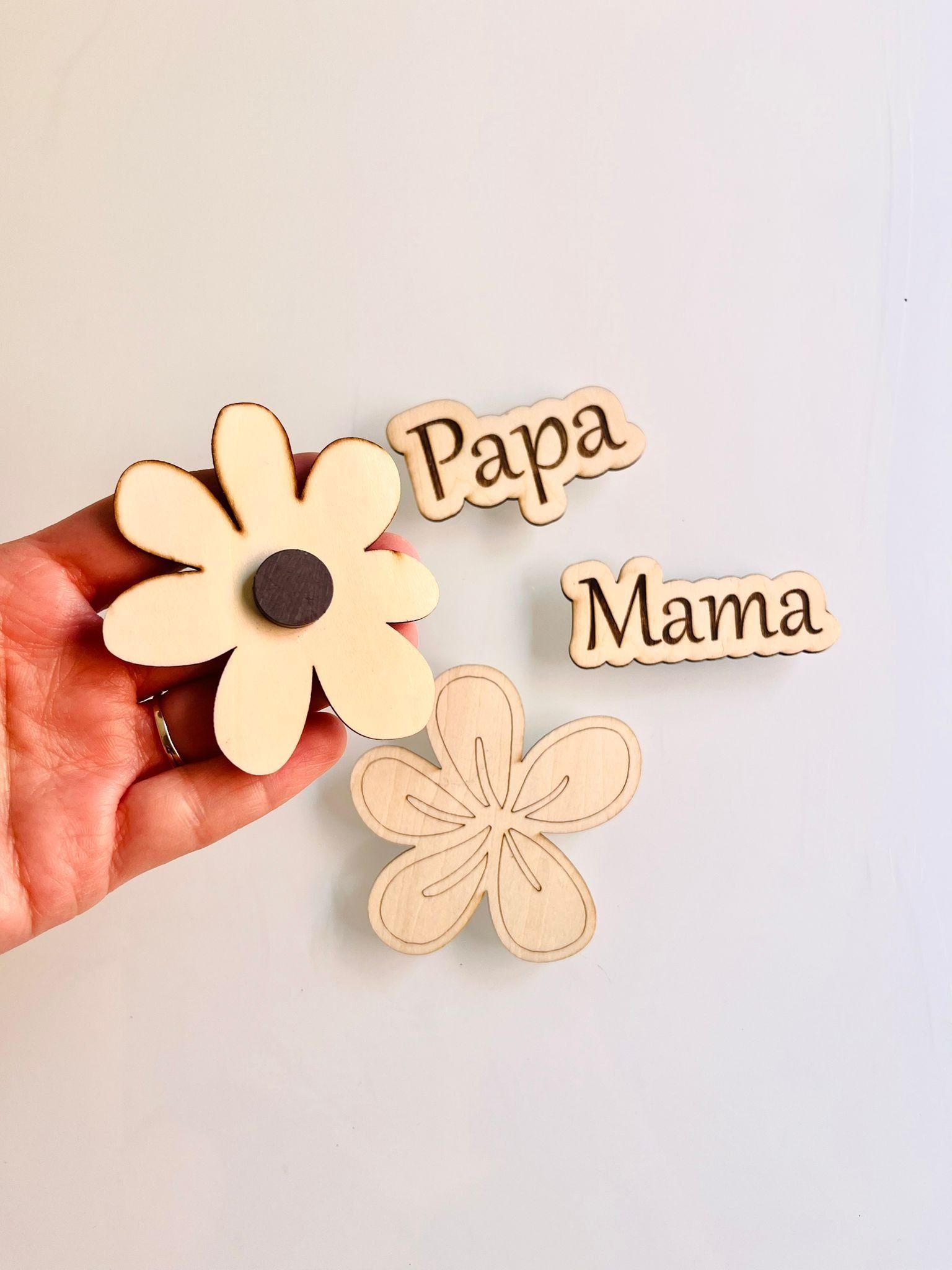 Una mano sostiene un imán de madera con forma de flor, con letreros de madera que dicen 