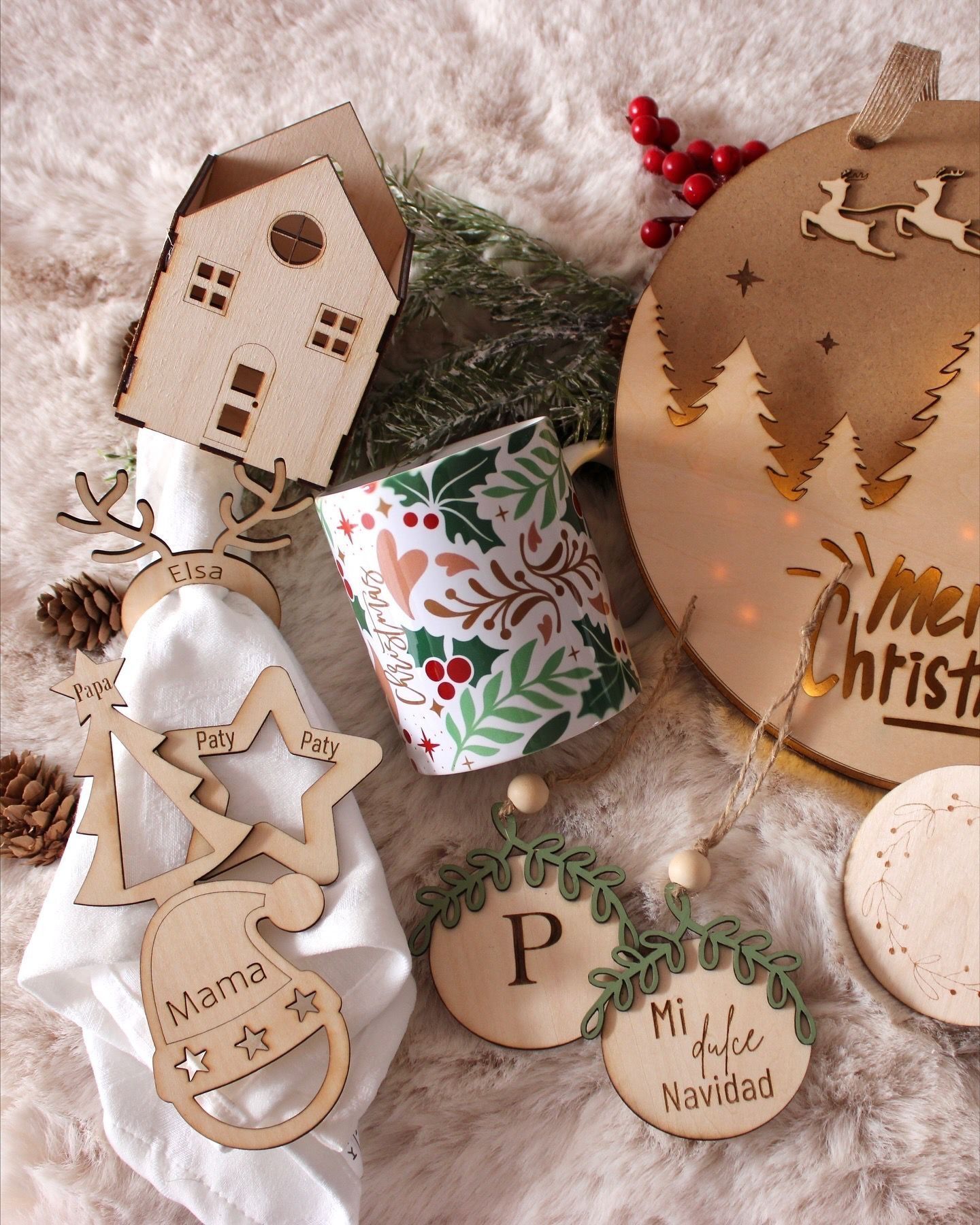 Una colección de adornos navideños de madera hechos a medida, que incluye adornos, una casa y una taza sobre una superficie blanca y esponjosa.