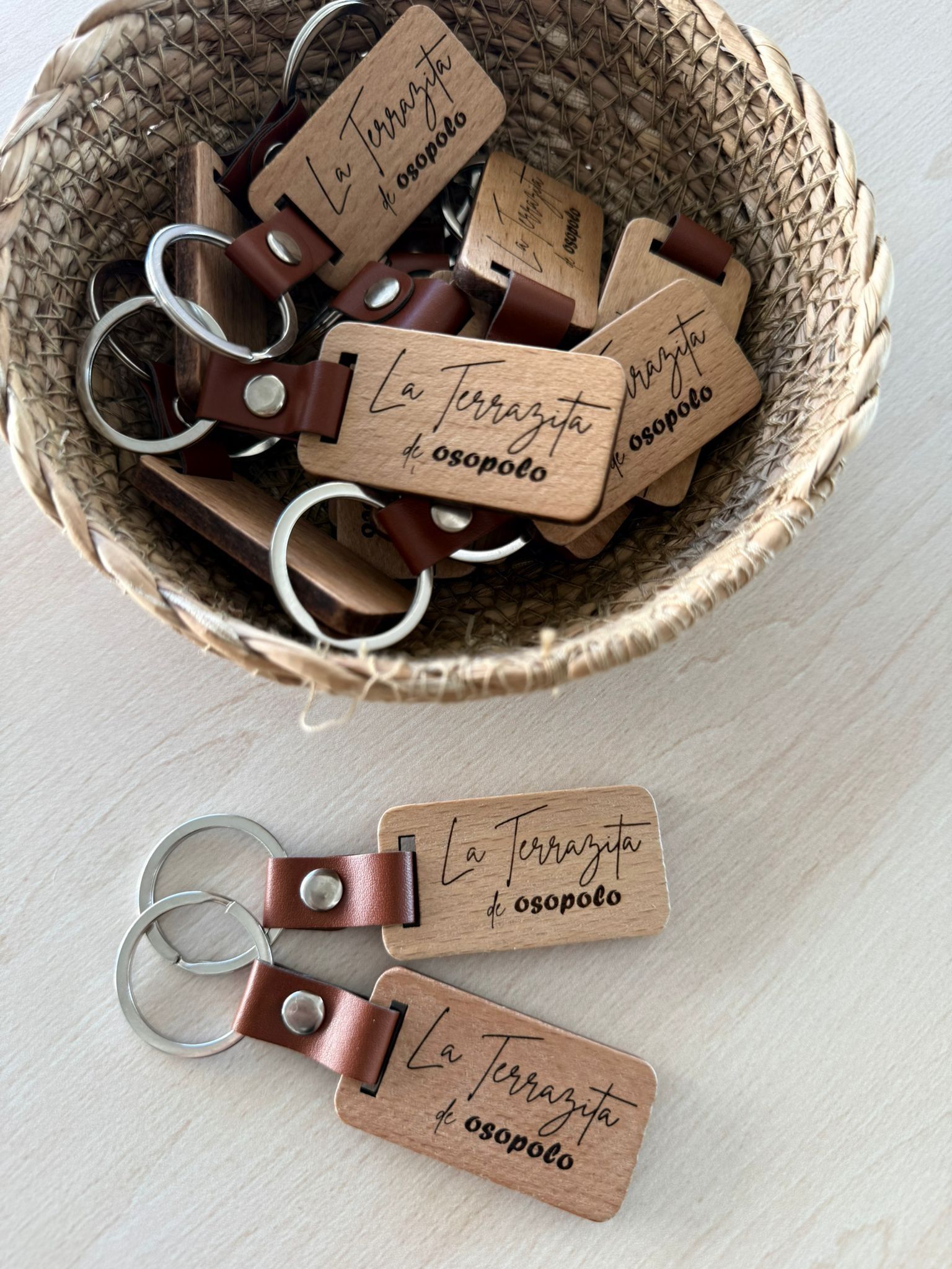 Una cesta tejida llena de llaveros de cuero marrón con texto grabado, además de dos llaveros idénticos que yacen delante.