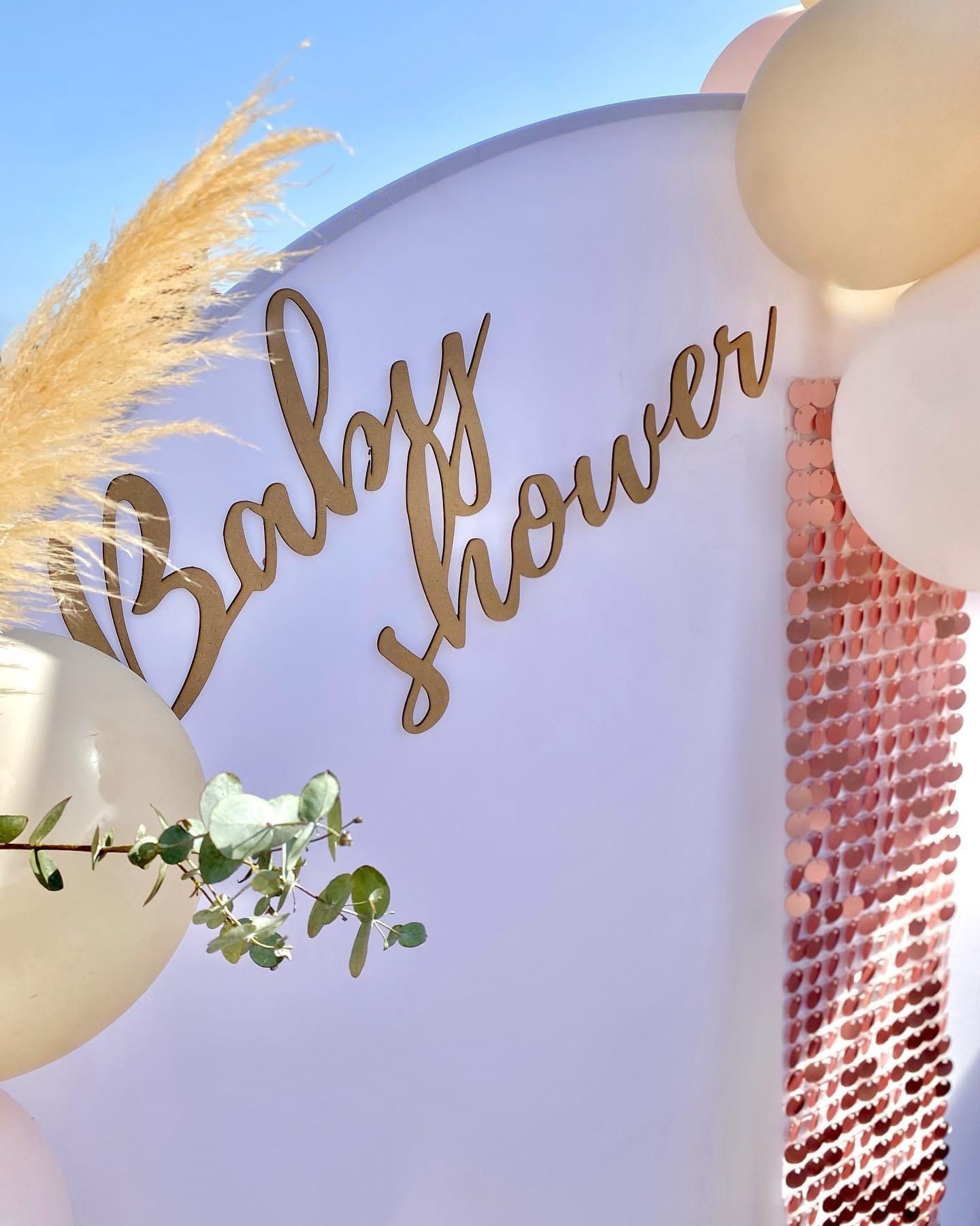 Un fondo circular blanco para baby shower decorado con globos beige, hierba de la Pampa, vegetación y una pared con brillo oro rosa.