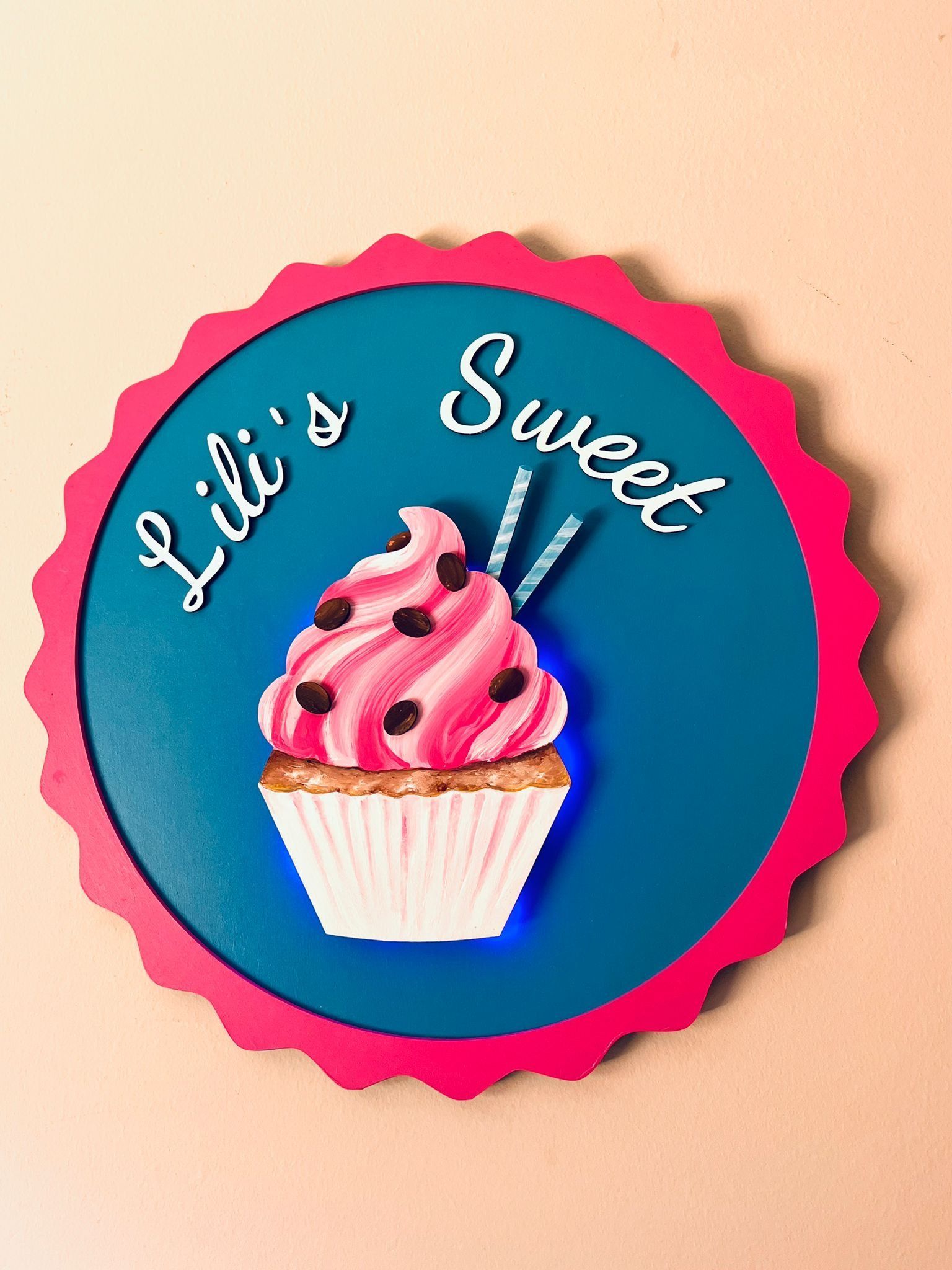 Letrero circular con borde festoneado rosa, fondo azul, ilustración de una magdalena y el texto 