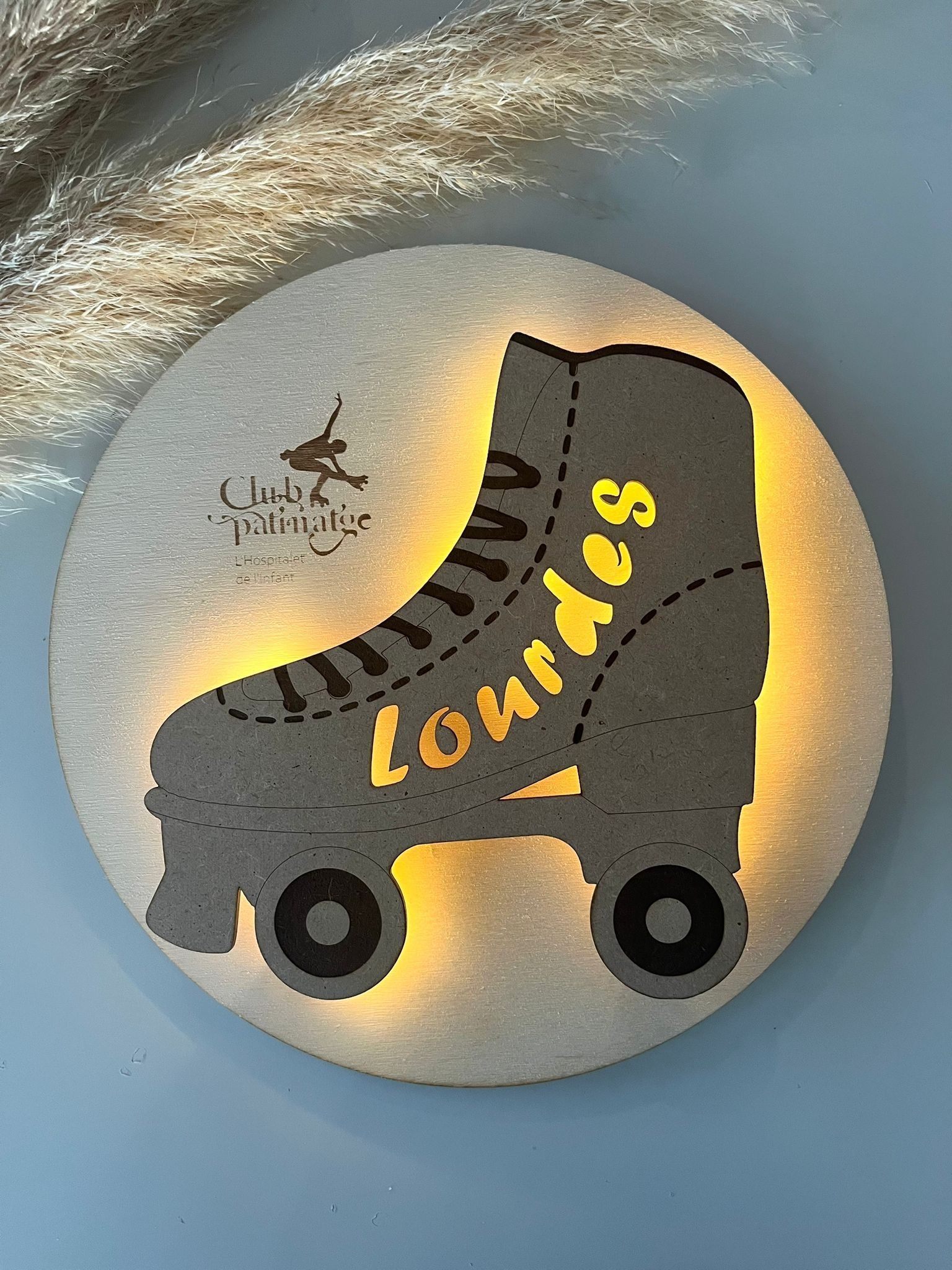 Una lámpara de pared circular, plateada y brillante, con la silueta de un patín y el nombre 