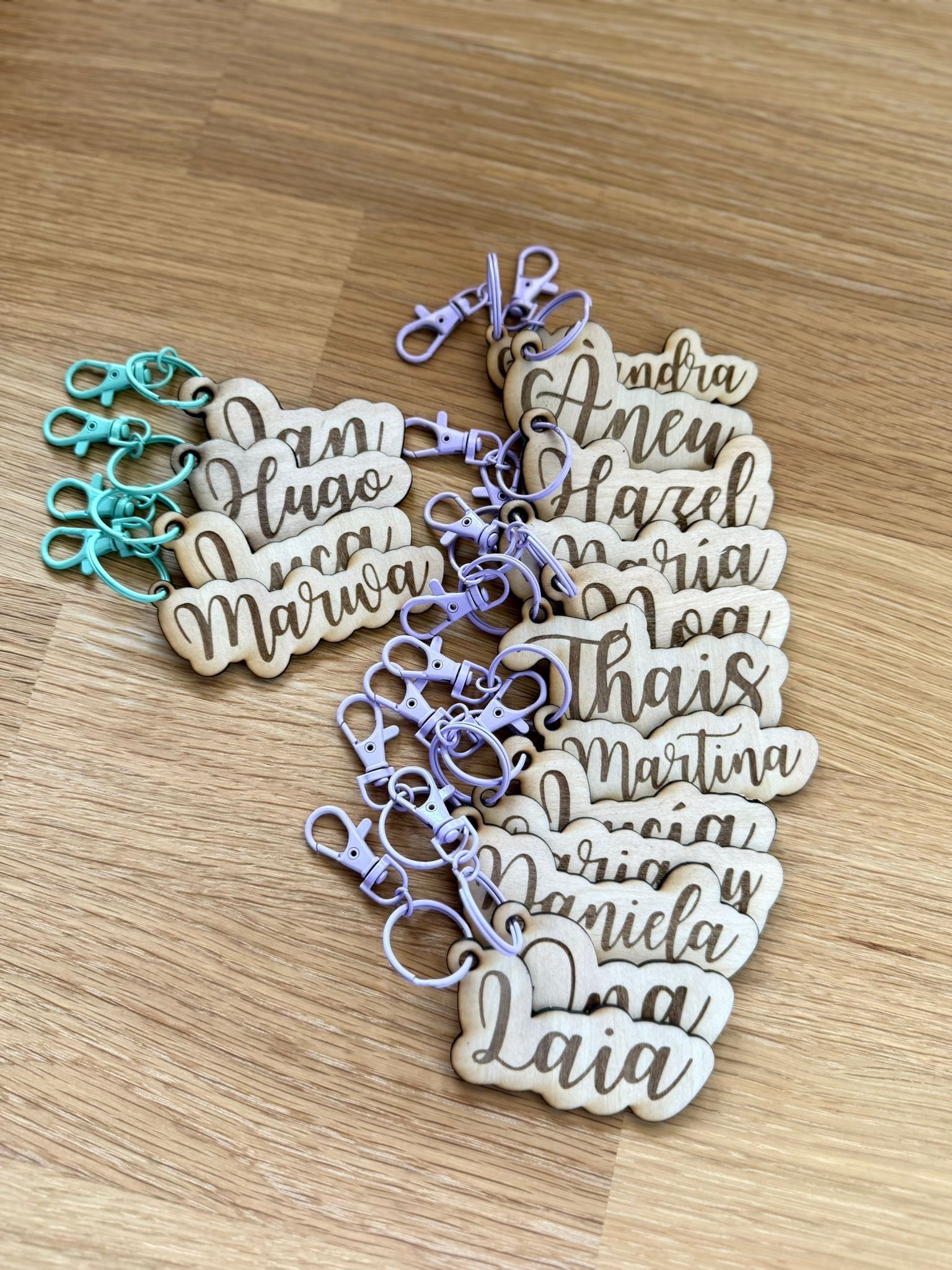 Varios llaveros de madera personalizados con nombres grabados, sujetos a cierres giratorios de color azul claro y lavanda.