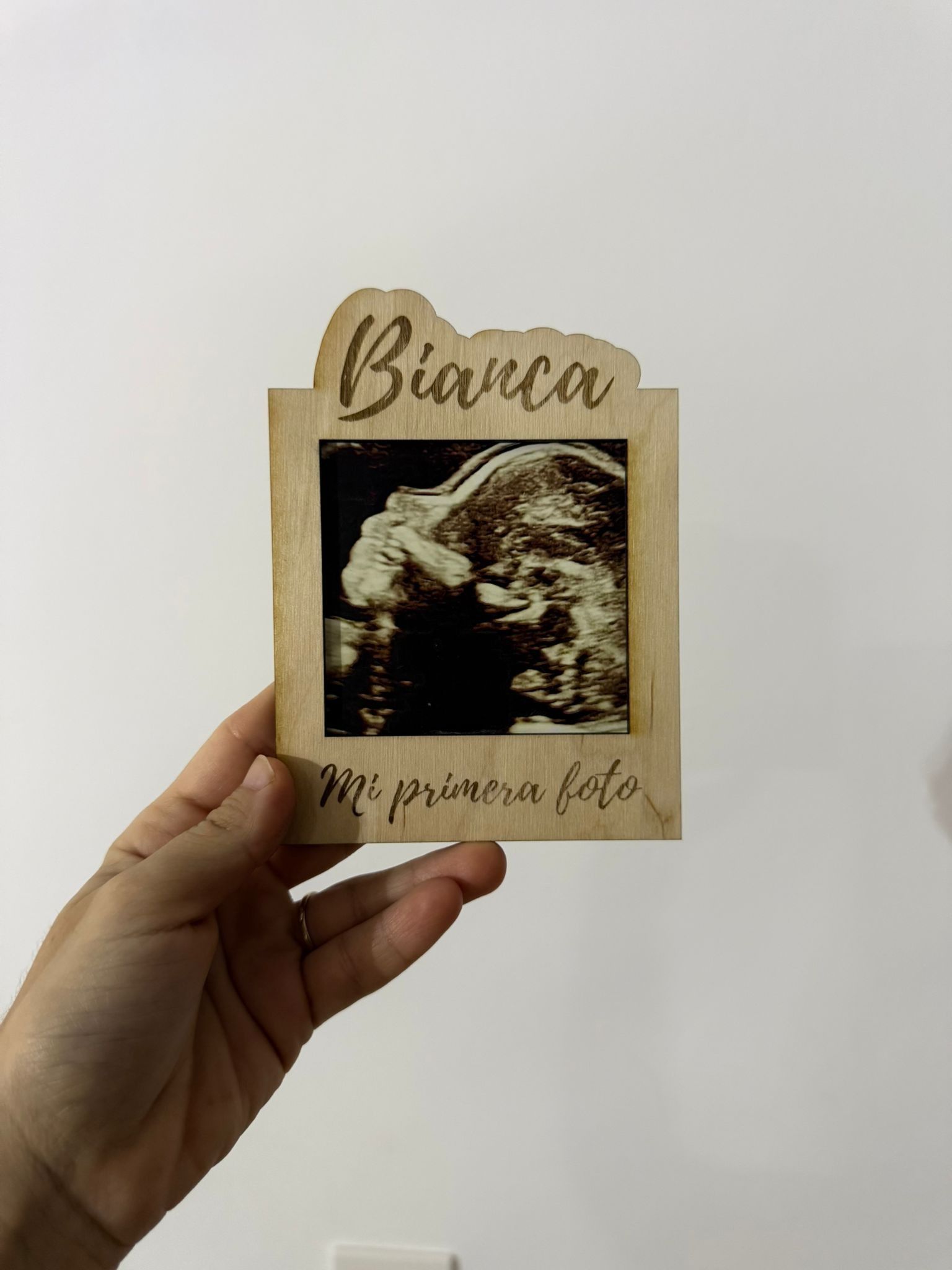 Una mano sostiene una placa de madera grabada con el nombre 