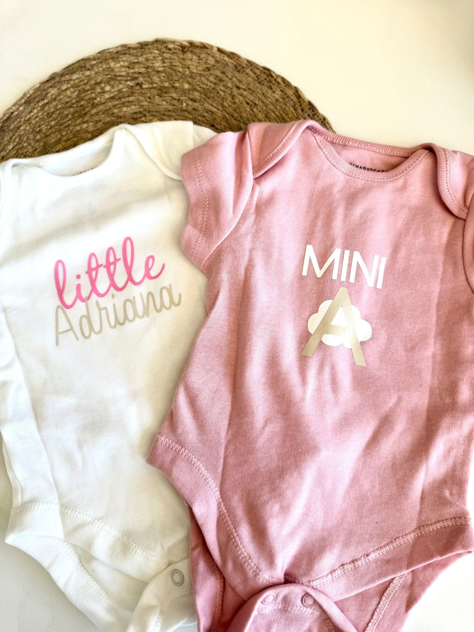 Dos bodys de bebé, uno blanco con la inscripción 