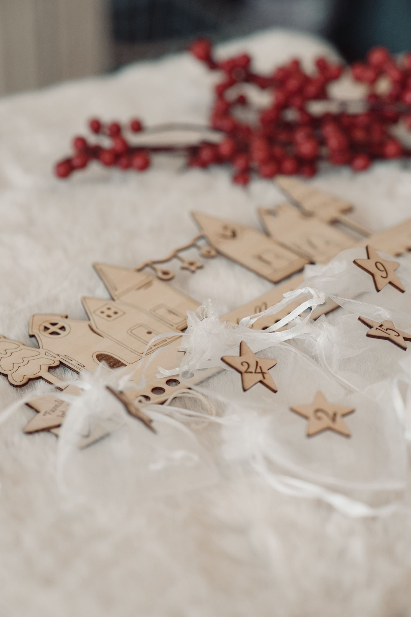 Calendario de Adviento con adornos de casas de madera, estrellas numeradas y bolsitas blancas transparentes sobre un fondo de bayas rojas.