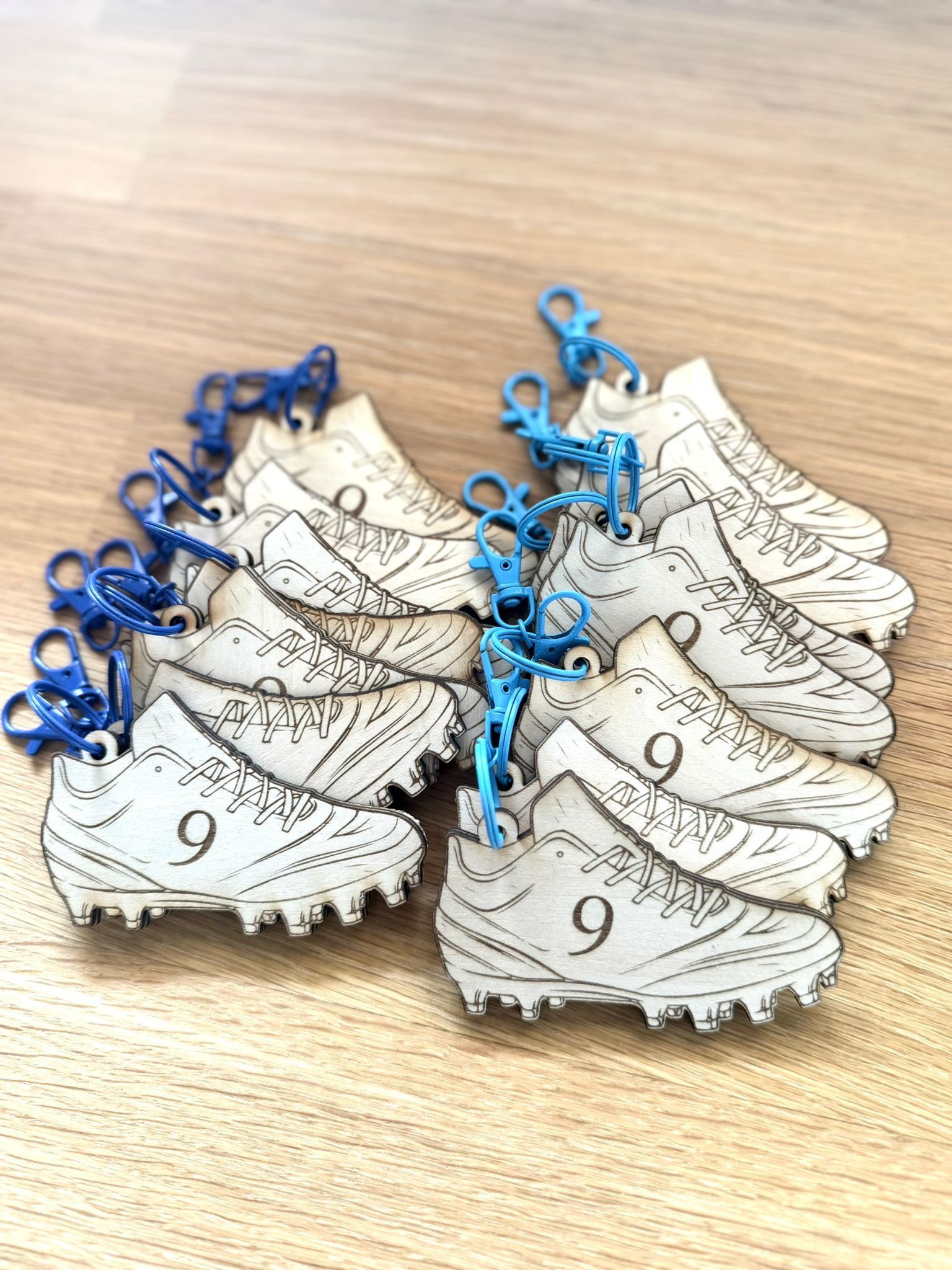 Un conjunto de llaveros de madera con forma de botas de fútbol, ​​cada uno grabado con el número 9 y sujeto a un broche de plástico azul brillante.