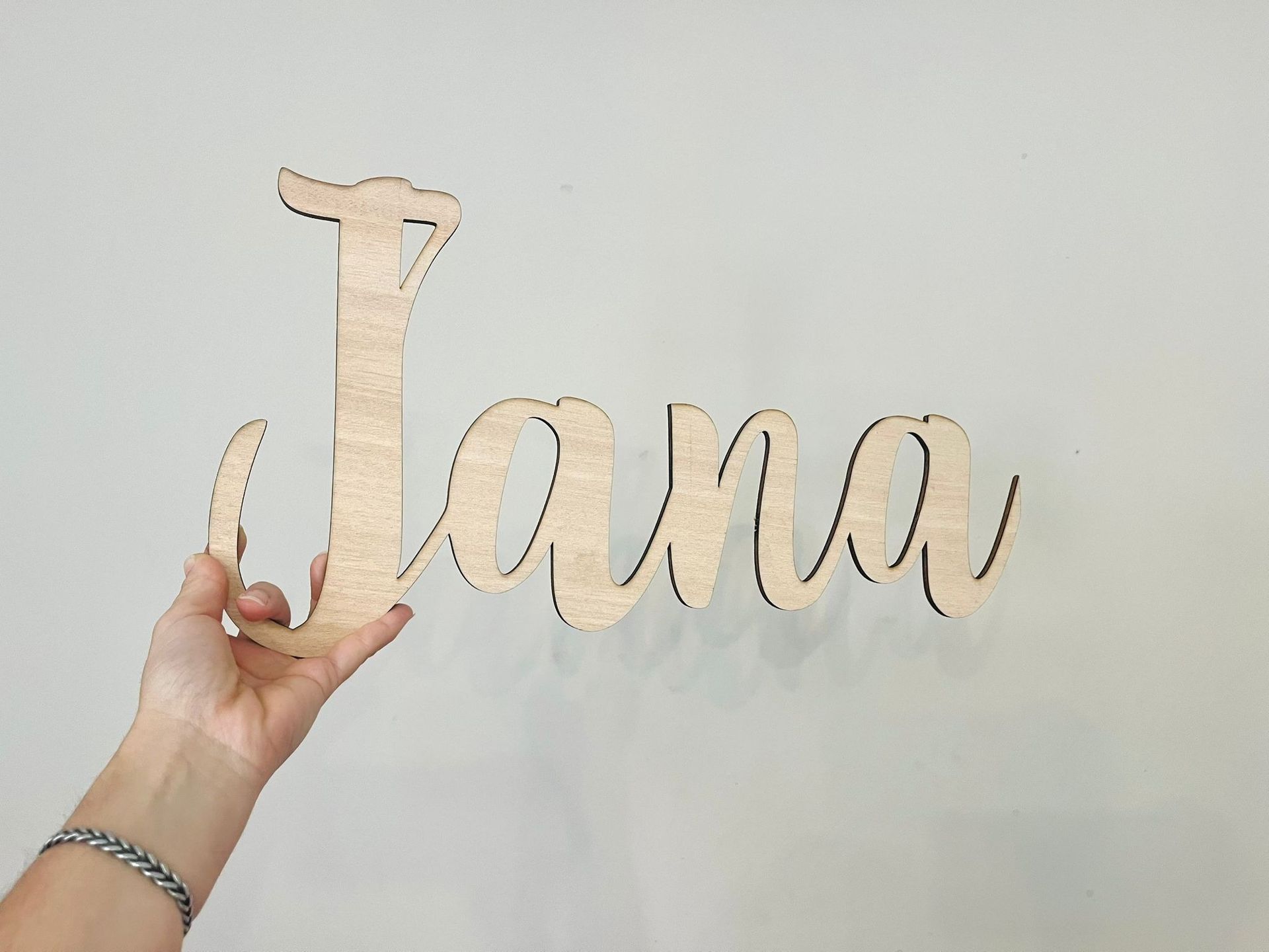 Una mano sostiene un cartel de madera personalizado, cortado con láser, con el nombre 