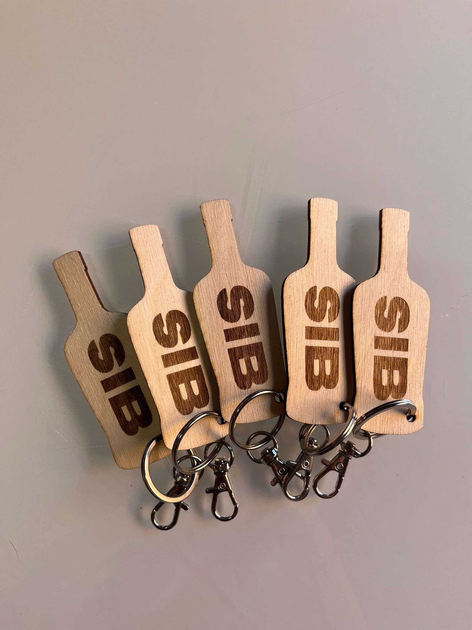 Cinco llaveros de madera de color claro con forma de botella, con las letras 