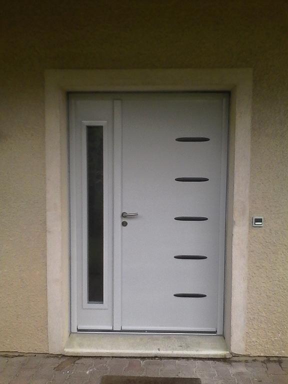 Porte blanche avec un panneau latéral et cinq barres horizontales noires. Encastrée dans un cadre de porte beige.