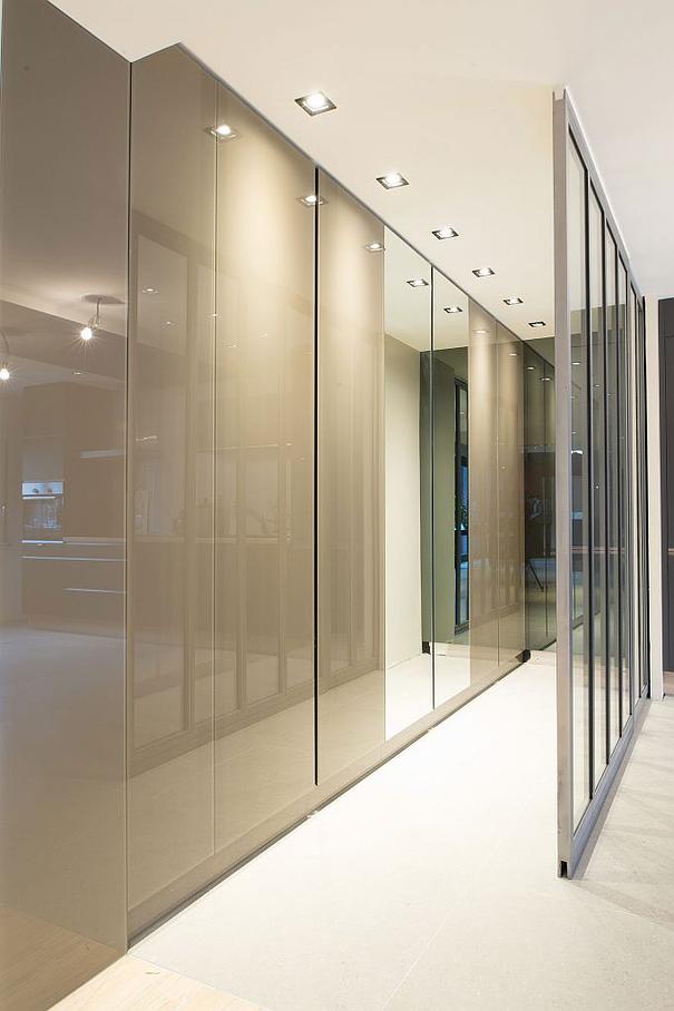 Couloir moderne avec placards taupe brillants, éclairage encastré et cloison vitrée.