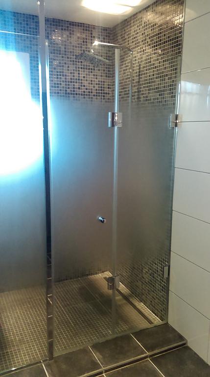 Cabine de douche en verre dépoli, mur carrelé de mosaïque et carrelage foncé au sol.