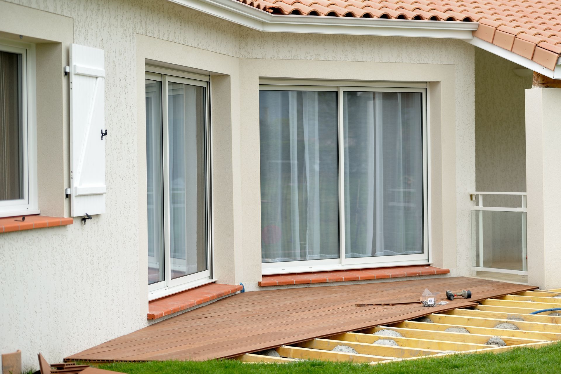Extérieur d'une maison avec portes coulissantes en verre, terrasse non aménagée et volets blancs.